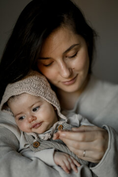 A mother gently holds her baby wrapped in soft knitwear, both sharing a quiet moment of calm connection.
