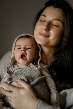 Mother holding baby while both yawn in cozy, warm indoor setting