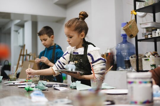 Young girl and boy paint small toys with care in bright art studio filled with creative tools and natural light