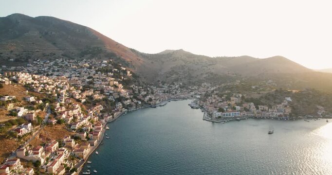 Aerial view of Simi town's terracotta rooftops cascading down to the turquoise bay, a yacht sailing on the water, Simi, Rhodes, Greece.