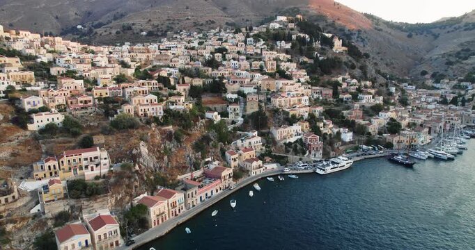 Aerial view of Simi town, showcasing houses on a hillside and boats along the harbor, creating a vibrant scene, Simi, Rhodes, Greece.