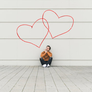 Digital composite of young man sitting at a wall with hearts