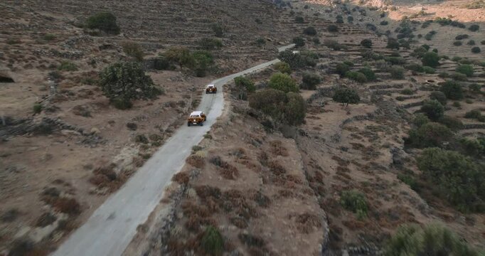 Aerial view of several vehicles driving along a winding road surrounded by dry terrain and sparse vegetation, Nikia, Kos, Greece.