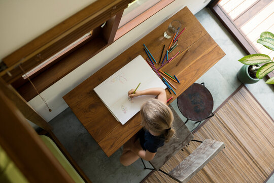 Little girl sitting at table drawing with crayons