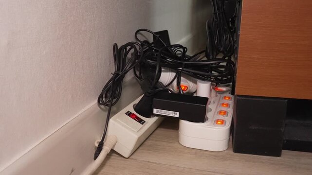 A realistic shot illustrating a common household fire hazard: the dangerous extension and 'daisy chaining' of multiple electrical power strips (multi-taps). The footage shows tangled cables connected
