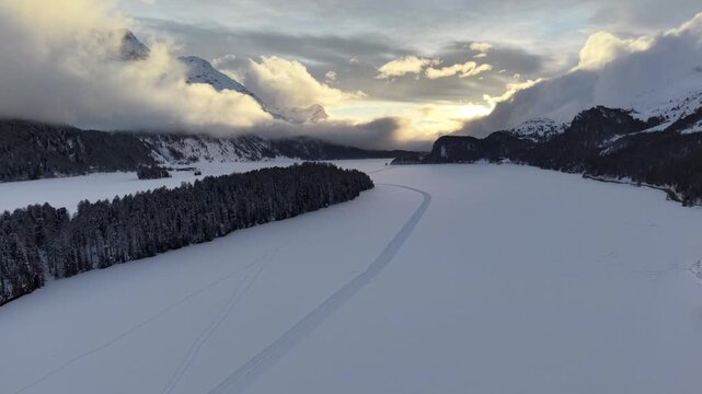 Aerial view of snow covered landscape, forests, and mountains under a cloudy sky, creating a serene winter scene, Sils im Engadin/Segl, Grigioni, Switzerland.