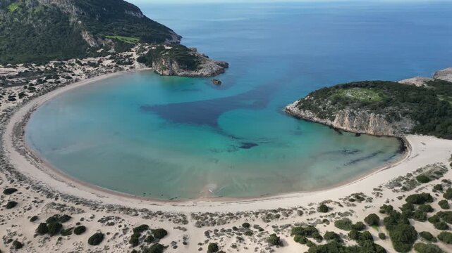 Aerial view of the turquoise waters of Voidokilia Beach surrounded by sandy dunes and lush greenery, creating a serene coastal landscape, Voidokilia Beach, Greece.