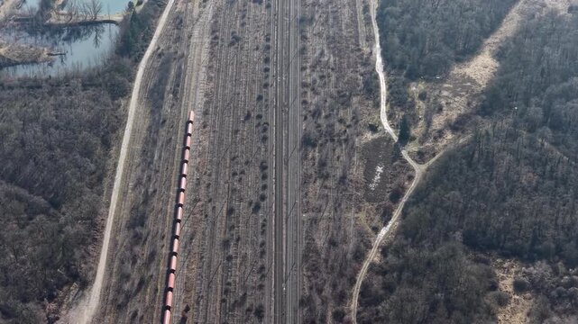 Aerial view of train tracks cutting through a pale landscape, bordering a dense forest and a small pond, Wittelsheim, Grand Est, France.