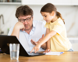 Father helps daughter do homework using laptop