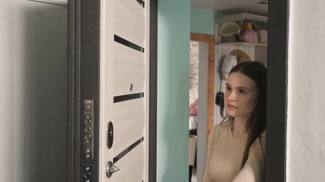 young caucasian woman at apartment door, hesitant expression while male courier holds parcel and clipboard, closeup on lock and peephole, homeowner inspects ID, verifies signature, checks door