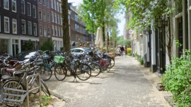 Blurry scene of amsterdam street with bicycles parked along tree-lined pathway and people walking in the distance under dappled sunlight, capturing urban life and greenery.