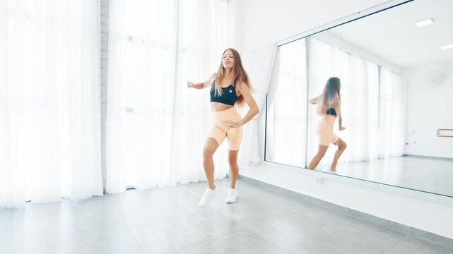 Young adult woman dances zumba in the bright airy room