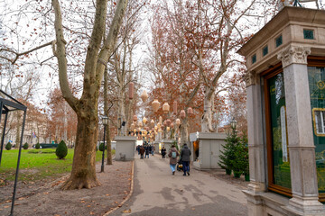 Park Zrinjevac decorated with hanging lights and small kiosks in Zagreb. Cozy winter atmosphere with pedestrians enjoying seasonal city decorations