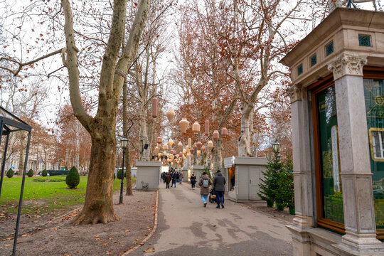 Park Zrinjevac decorated with hanging lights and small kiosks in Zagreb. Cozy winter atmosphere with pedestrians enjoying seasonal city decorations