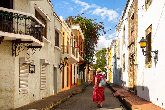 A traveler in a red dress wanders down a sun-drenched, historic street in Santo Domingo, framed by colonial architecture and charming balconies.