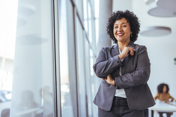 Confident Businesswoman in Grey Suit Smiling by Large Window in Modern Office