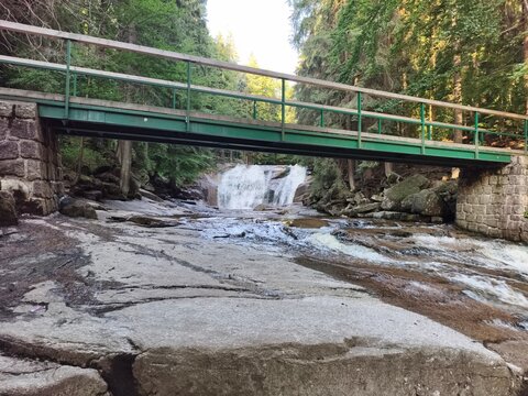 walkway crossing stony riverbed scene, bridge spanning rugged stream with waterfalls and textures