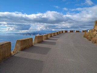 Fototapeta premium Curved oceanfront highway featuring stone barriers and dramatic cloud formations for cinematic visuals