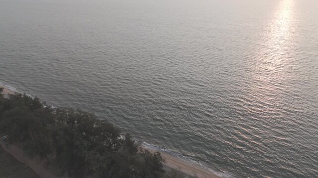 Aerial drone view of Querim Beach, North Goa, revealing a long sandy coastline with scattered rocky outcrops, rows of trees, and the Arabian Sea under soft winter evening light