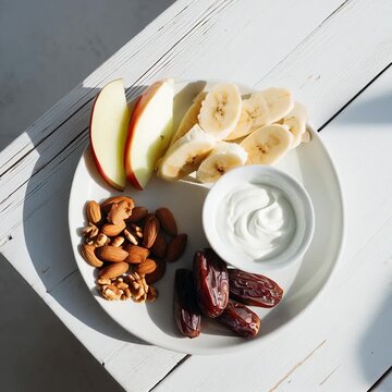 Gesundes Fr&uuml;hst&uuml;ck mit Joghurt, Banane, Apfel, N&uuml;ssen und Datteln auf hellem Holzuntergrund. Ausgewogene Ern&auml;hrung f&uuml;r Fitness, Sport und Abnehmen. Clean Eating, nat&uuml;rlich und energiereich.