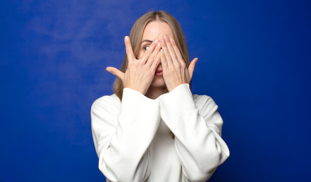 covering face with hands, peeking between fingers with surprised expression and looking to the side