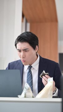 会社の休憩中に時間がなくてオニギリなどを急いでオフィスで食べる忙しい男性のビジネスシーン縦動画