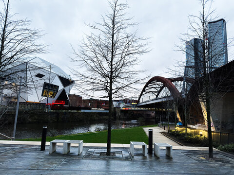 Urban riverside scene in Manchester UK with modern architecture bridge and winter trees. Aviva Studios, home of Factory International.