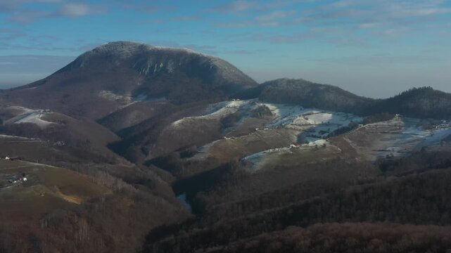 Aerial view of a snow-dusted mountain range with contrasting dark forests and patches of white snow under a clear blue sky, Holbav, Brasov, Romania.