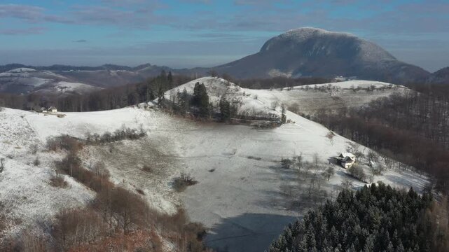 Aerial view of snow covered hills with scattered houses and bare trees, creating a winter wonderland landscape, Holbav, Brasov, Romania.