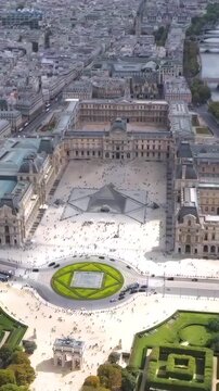Aerial vertical drone view spinning over the Louvre, Tuileries Garden, Seine River and Place du Carrousel surrounded by the historic Parisian skyline.