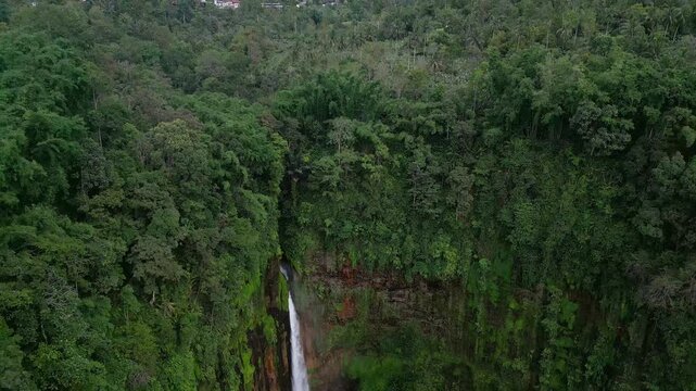 Drone video of a powerful waterfall crashing through dense jungle beneath Semeru Volcano. Dark volcanic cliffs, rising mist, and heavy water flow define this dramatic tropical landscape in East Java
