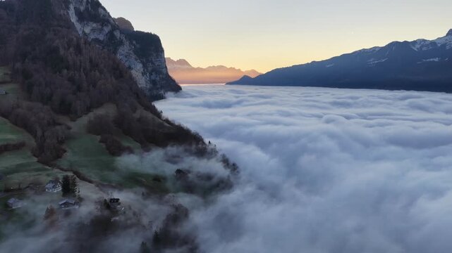 Aerial sunrise over Walensee lake with fog inversion filling alpine valley in Switzerland.