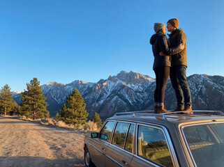 A young couple in love sit on a camper, admiring the view of the mountains and freedom