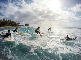 A surfer rides his board alongside friends as they ride a foaming wave against a cloudy sky on a sunny day on an island