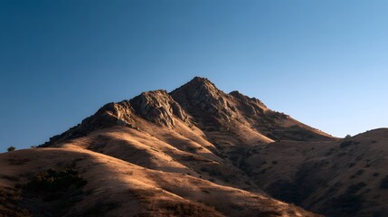 Fototapeta premium Golden light illuminates a rugged mountain ridge under a clear blue sky at dawn or dusk