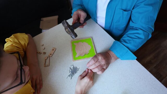 Close up of hands using a hammer to assemble a wooden puzzle on a green base, crafting, focus, DIY project with small parts and tools.