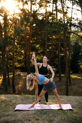 Female yoga instructor helping woman with standing yoga pose outdoors at sunset. Alignment, balance, flexibility and mindful practice.