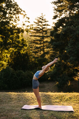 Woman practicing standing yoga backbend outdoors at sunset. Flexibility, posture, balance and mindful wellness lifestyle concept.