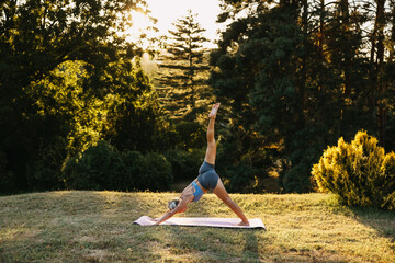 Woman practicing three-legged downward dog yoga pose outdoors at sunset. Balance, strength, flexibility and mindful movement concept.