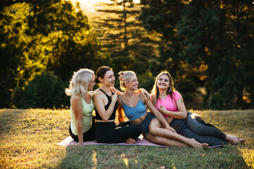 Group of women in activewear relaxing together on yoga mats in a park at sunset. Wellness, friendship, outdoor yoga retreat, positive lifestyle and community concept.