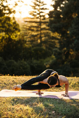 Athletic woman practicing advanced side arm balance yoga pose outdoors at sunset. Strength, flexibility and focused yoga practice in nature.