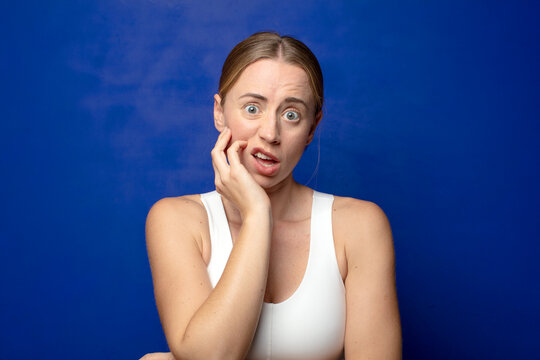 blonde woman open-mouthed in shock and disbelief, with hand on cheek and arm crossed, feeling stupefied and amazed