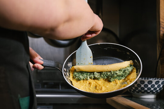 Chef preparing omelet with spinach and cheese filling