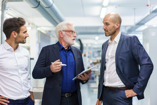 Senior male manager with colleagues discussing over digital tablet while standing at illuminated factory