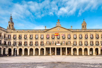 Fototapeta premium Wide view of Spain square in Vitoria-Gasteiz, featuring neoclassical arcaded facades, balconies and an open stone square under a bright blue daytime sky. High quality photo