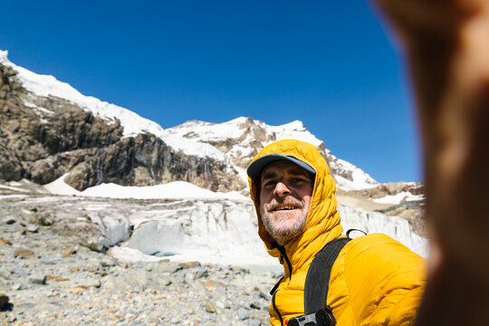 Smiling man taking selfie against snowcapped mountain