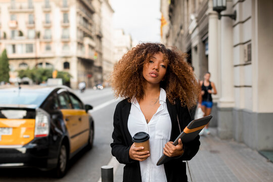 Young woman with laptop bag and coffee to go in the city, missing the taxi