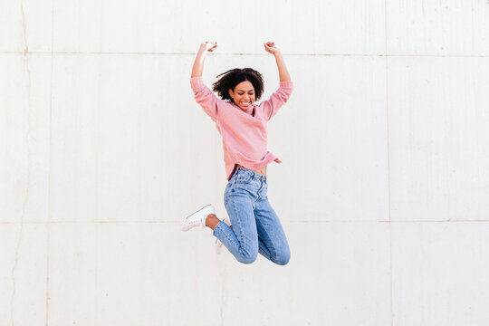 Happy young woman jumping in the air against light background