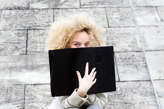 Blond woman with ringlets hiding behind black folder