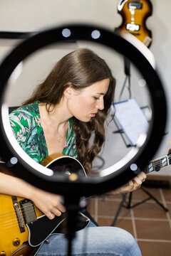 Young woman with webcam light playing guitar while sitting at home
